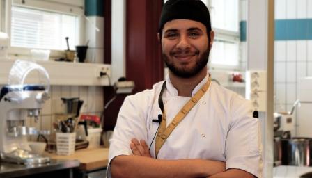 Ahmed Hussein katsoo kameraa leipuritakki ja huivi päällään.