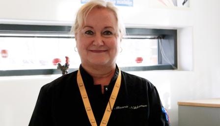 Maarit Nikkanen katsoo kameraan ja hymyilee. Hänellä on päällään musta kokkitakki ja kaulassa Omnian keltainen avainnauha.