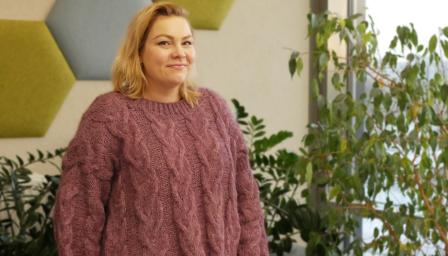 Hanna Tenhunen seisoo värikkään seinän ja kasvien edessä ja katsoo kameraan.