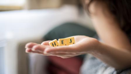 Etualalla käsi, jossa kolme kirjainta jotka muodostavat sanan "Hej".