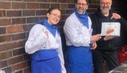 Kolme henkilöä essut päällä poseeraavat talon edustalla.