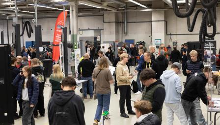 Suuri määrä nuoria ihmisiä tutustumassa autoalan edustajien ständeihin. Ympäristönä on autohalli.