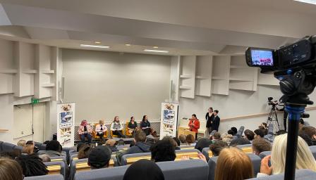 Yleisö seuraa vaalipaneelia auditorioympäristössä. Panelistit istuvat lavalla Omnian mainosjulisteiden edessä, ja esiintyjä seisoo puhujanpöntössä. Tilaisuutta taltioidaan videokameralla, joka näkyy kuvan oikeassa laidassa.