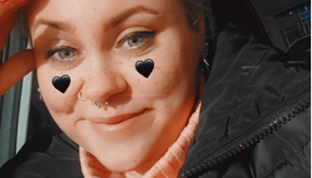 Helena Metsänranta katsoo kameraan. Hänellä on poskipäissä piirretyt mustat sydämet. Hän hymyilee.