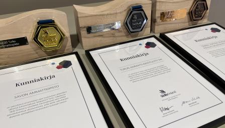 Kuvassa kunniakirjoja ja palkintoja kolme kappaletta.