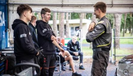 Moottoriurheiluopiskelijat juttelevat ohjaajan kanssa kilpatallilla.