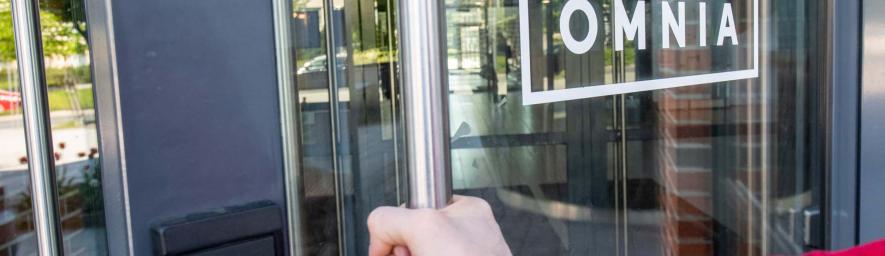 Henkilö avaa lasiovea, jossa on Omnian logo.