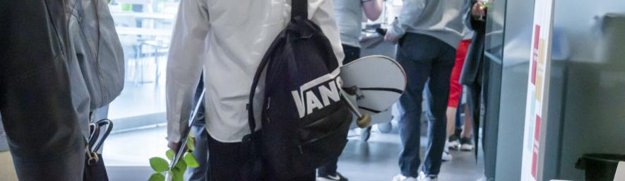 Henkilö kävelee poispäin. Kädessään hänellä on ruusu ja skeittilauta.