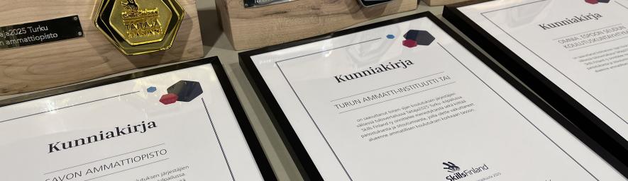 Kuvassa kunniakirjoja ja palkintoja kolme kappaletta.