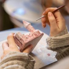 Taidepajan opiskelija maalaa pientä keraamista linnaa.