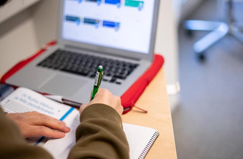 Lukio-opiskelija kirjoittaa muistiinpanoja luokassa läppärin ääressä.