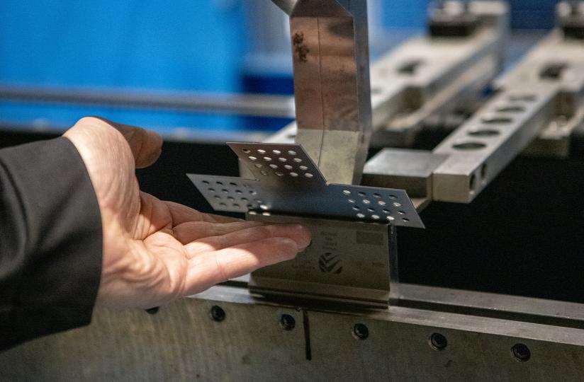 Metallintyöstöprosessi: henkilön käsi pitelee rei'itettyä metallilevyä taivutuskoneessa teollisuusympäristössä.