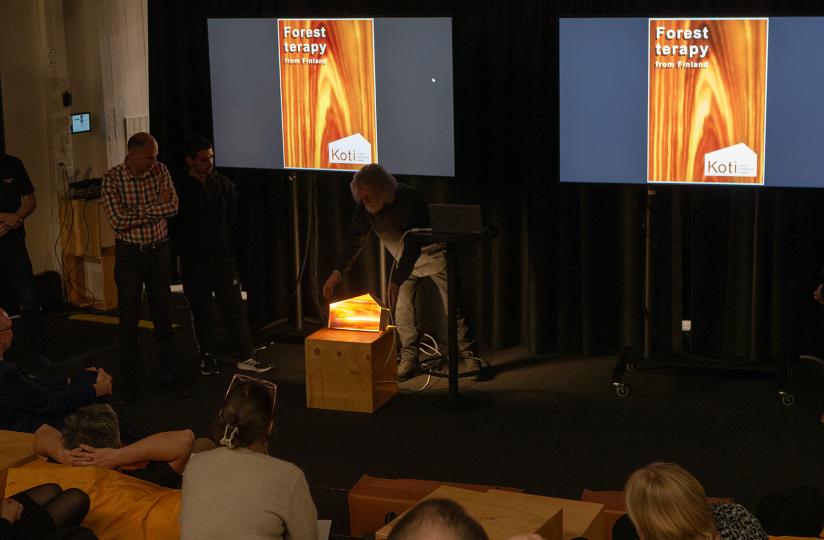 Ryhmä esittelee Forest Therapy -valokonseptia, ja puukuution päälle asetettu valaistu prototyyppi hehkuu lämpimänvärisenä.