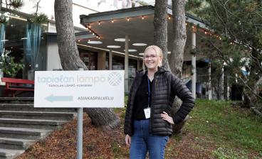 Emma Lahtinen seisoo rakennuksen edessä vieressään kyltti, jossa lukee Tapiolan Lämpö -konserni, asiakaspalvelu.