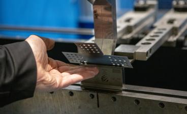 Metallintyöstöprosessi: henkilön käsi pitelee rei'itettyä metallilevyä taivutuskoneessa teollisuusympäristössä.