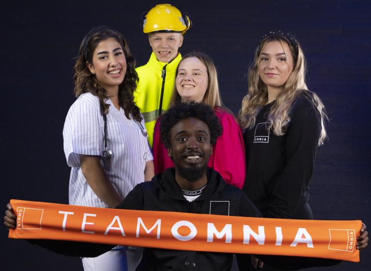 Ryhmä ammattiasuisia opiskelijoita näyttää oranssia huivia jossa lukee TeamOmnia.