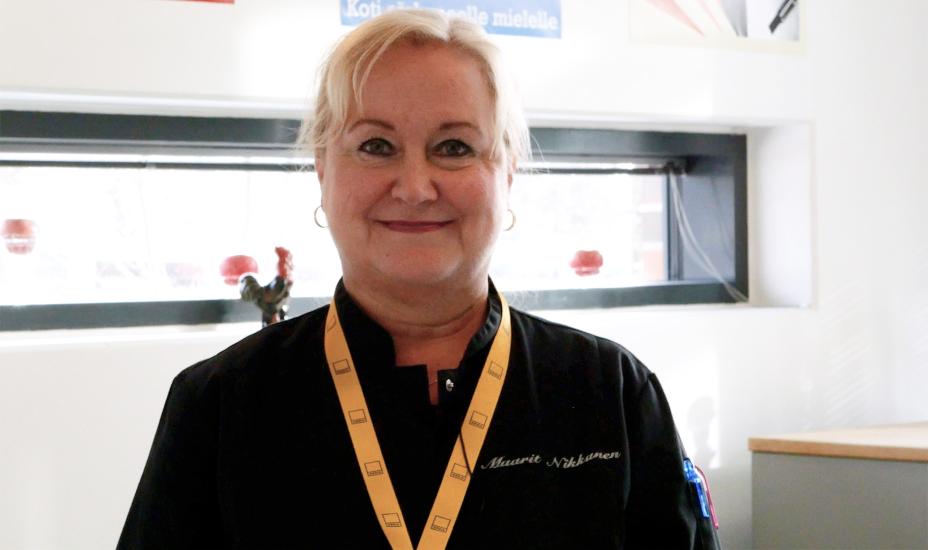 Maarit Nikkanen katsoo kameraan ja hymyilee. Hänellä on päällään musta kokkitakki ja kaulassa Omnian keltainen avainnauha.