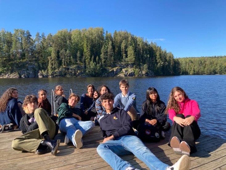 Genoese students sitting on a platform by a lake.
