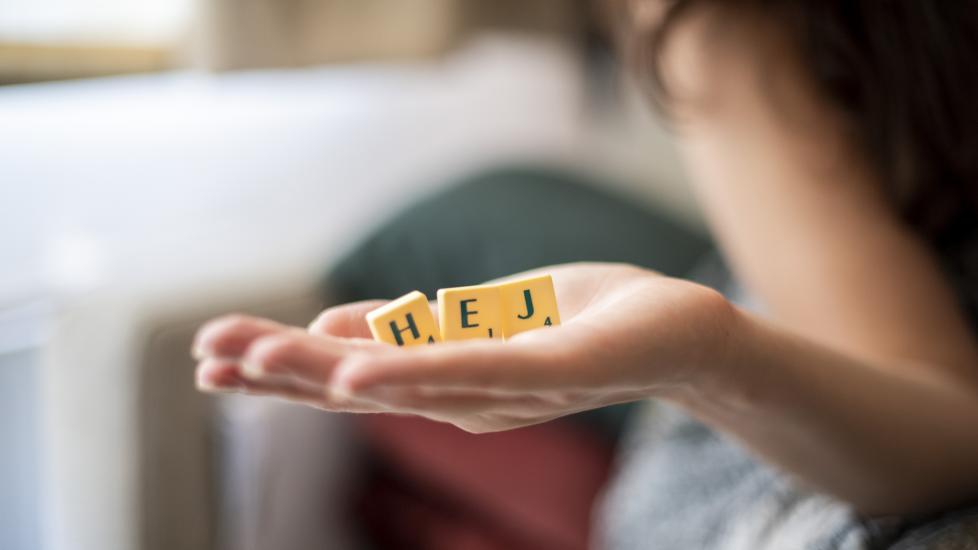 Etualalla käsi, jossa kolme kirjainta jotka muodostavat sanan "Hej".