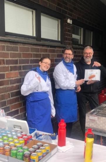 Kolme henkilöä essut päällä poseeraavat talon edustalla.