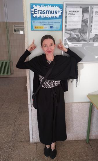 Milka poseeraa Erasmus+ -julisteen vieressä paikallisen koulun tiloissa.