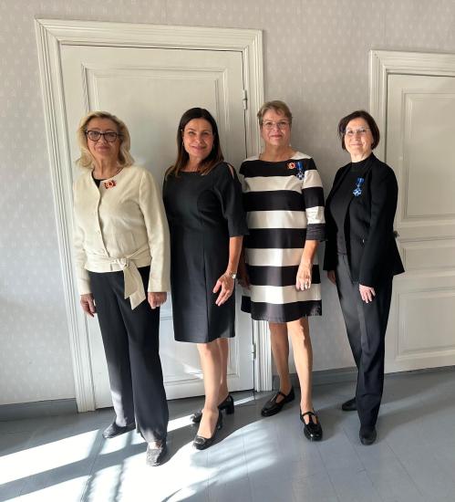 Neljä naista seisoo vierekkäin juhlavassa sisätilassa. Heillä on yllään mustavalkoisia asuja, ja kahdella heistä on rinnassaan huomionosoitusmerkki.