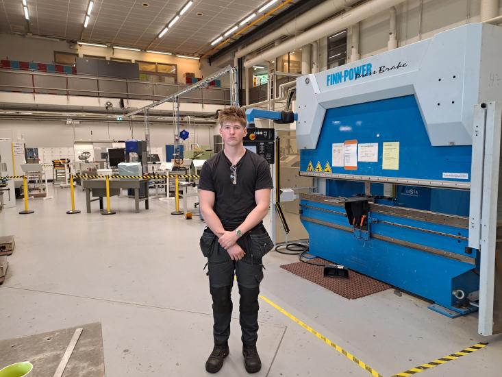 Kone- ja tuotantotekniikan opiskelija seisoo työpajassa suuren sinisen Finn-Power-puristimen edessä.