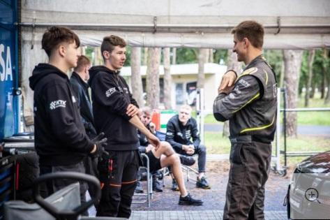 Moottoriurheiluopiskelijat juttelevat ohjaajan kanssa kilpatallilla.