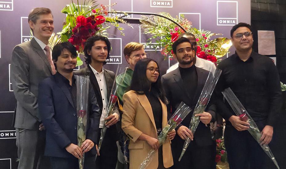 Joukko ihmisiä seisoo kukat käsissä kukkakaaren alla ja hymyilee. Taustalla on Omnian logoilla varustettu seinä.