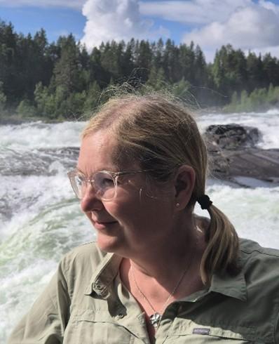 Kouluttaja Pirkko Taipaleen kuvan taustalla koski ja metsää.