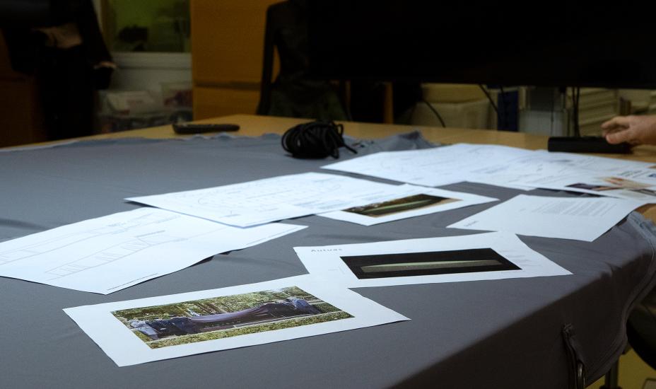 Pöydälle levitetyn kankaan päällä on papereita, joissa on teoksen suunnitelmat.