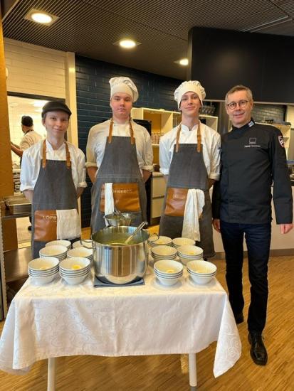 Kolme opiskelijaa ja yksi opettaja seisovat tarjoilupöydän takana kokkivaatteet päällä.