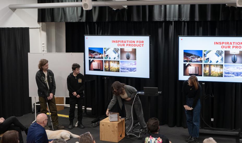 Nelihenkinen ryhmä esittelee valon rakennetta havainnollistavaa 3D-mallia kahdella näytöllä, ja valaisinprototyyppi on valaistuna edessä.