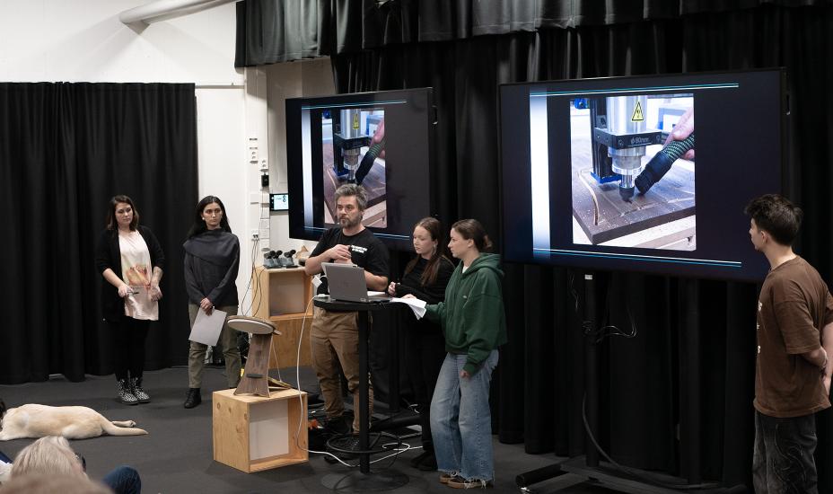 Opiskelijat ja ohjaaja esittelevät CNC-jyrsintään liittyviä työvaiheita kahdella suurella näytöllä.