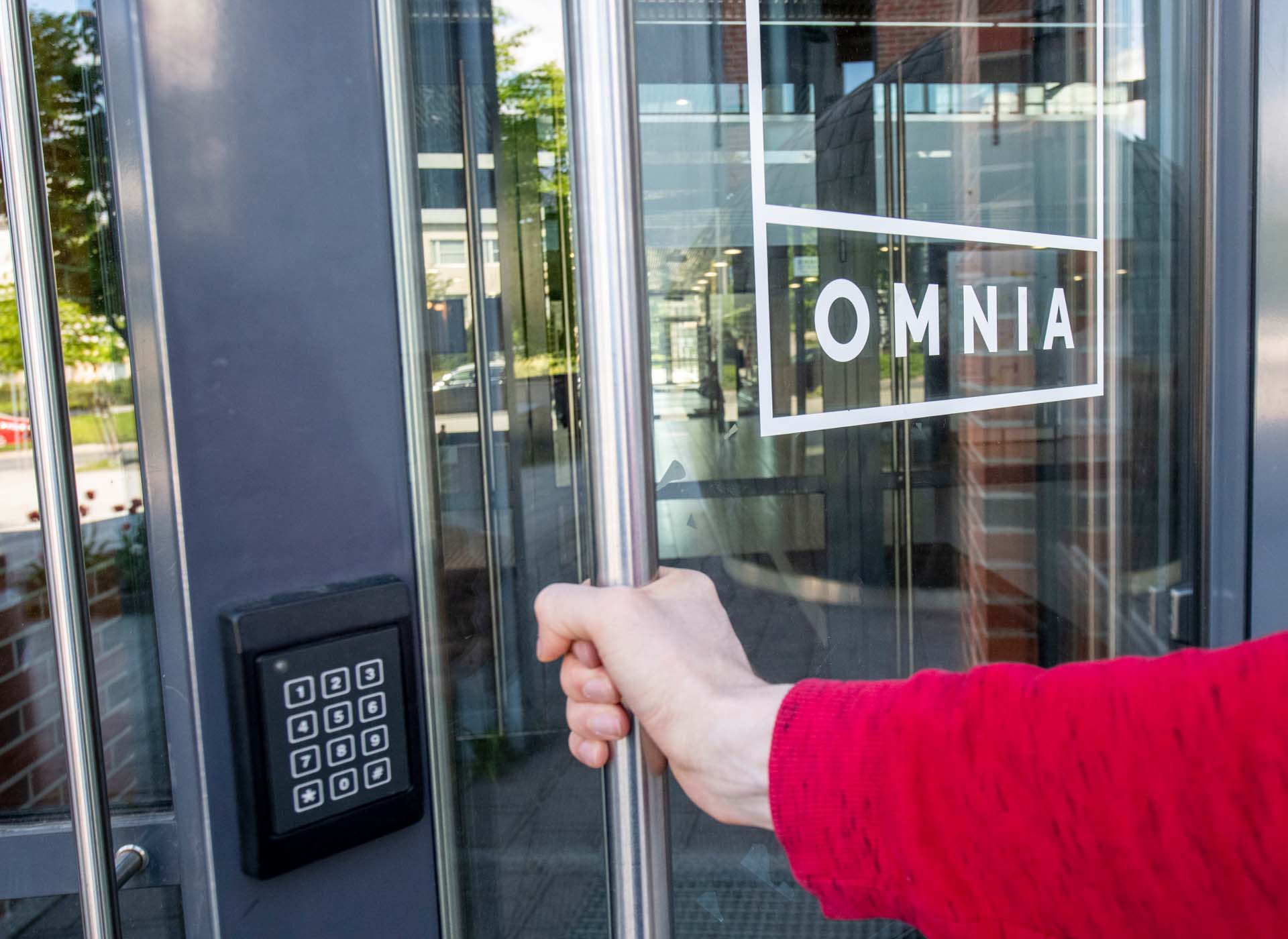 Henkilö avaa lasiovea, jossa on Omnian logo.