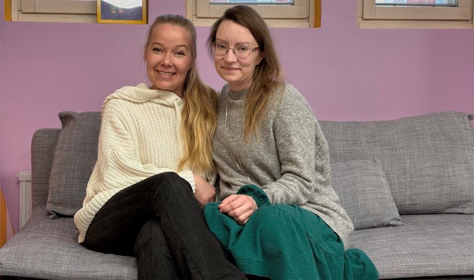 Kaksi henkilöä istuu vierekkäin sohvalla ja hymyilee kameralle sisätilassa.