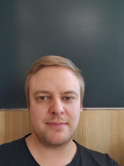 Henkilö katsoo kameraan sisätilassa tumman seinän edessä.