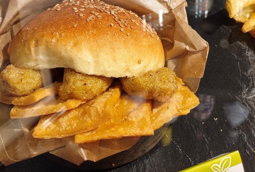 Lähikuva vegaanisesta burgerista, jonka välissä on perunaa ja kastiketta.