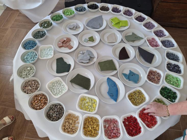 Pöydälle on aseteltu eri värisiä mosaiikkipaloja ja materiaalinäytteitä pieniin astioihin.